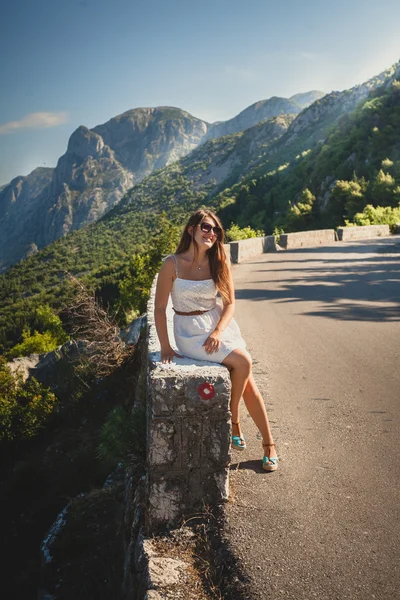 Young woman sitting on side of the high mountain road at sunny d — Stock Photo, Image