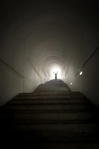 Person standing in the end of tunnel at light beam with hands ra — Stock Photo, Image