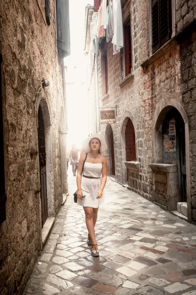 Женщина в белом платье ходит по узкой улочке древнего города — стоковое фото