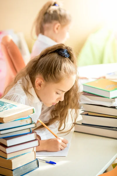 Brunetka dziewczynka siedzi w klasie i pisanie w Zeszyt — Zdjęcie stockowe