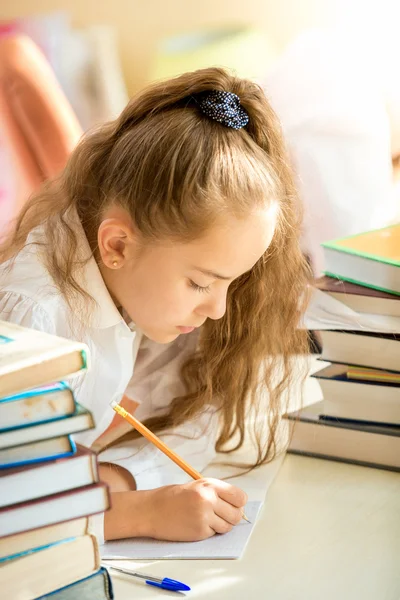 Brunett skolflicka omgiven av böcker gör läxor — Stockfoto