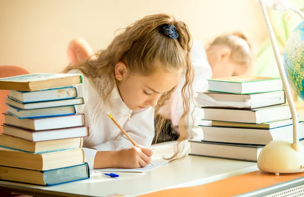 Estudante concentrada cercada por livros fazendo lição de casa — Fotografia de Stock