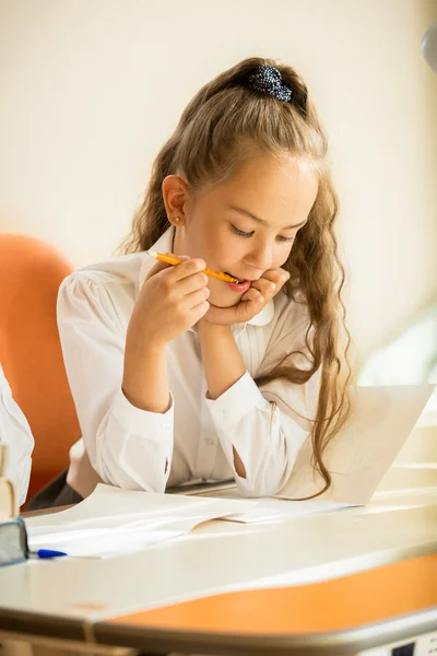 Retrato de la colegiala masticando lápiz mientras hace la tarea —  Fotos de Stock