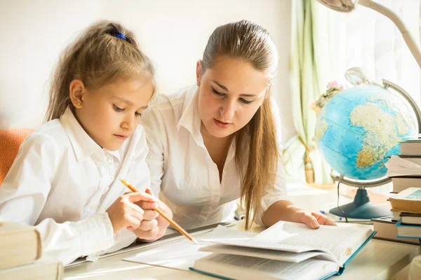 Mamma sitter med dotter på skrivbord och förklara uppgiften hemma — Stockfoto