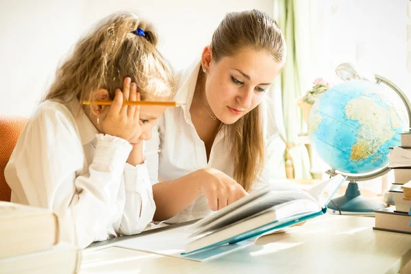 Мать и дочь читают учебник во время выполнения домашних заданий — стоковое фото