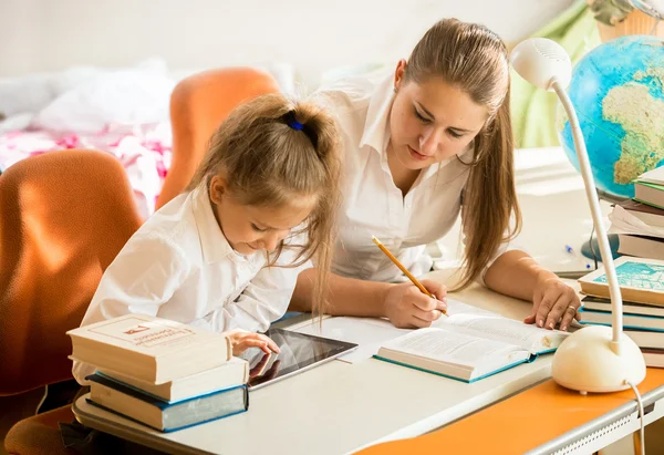 Chica con madre mirando en la tableta cómo hacer la tarea —  Fotos de Stock