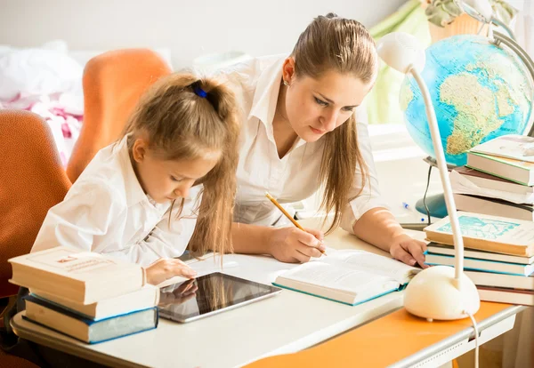 Chica usando tableta digital, mientras que la madre haciendo la tarea en lugar de —  Fotos de Stock