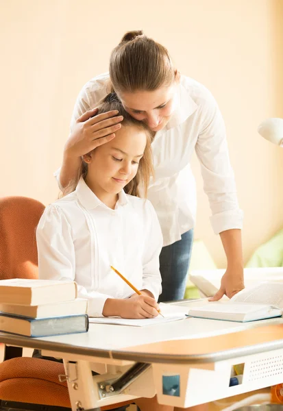 Jeune mère louant fille faire des devoirs au bureau — Photo