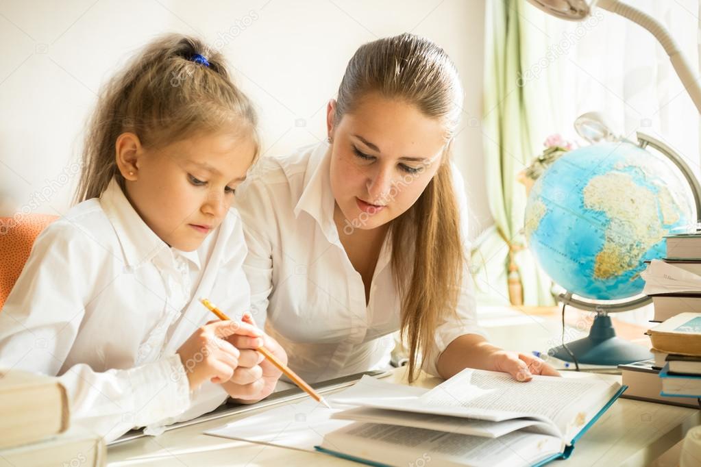 Mother sitting with daughter at desk and explaining task at home