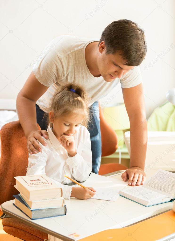 young father looking at daughter doing homework