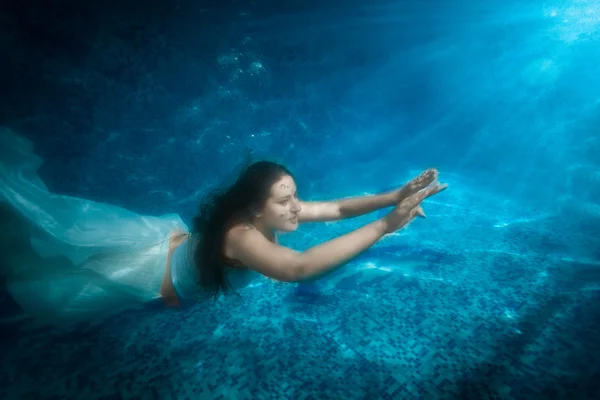 Hermosa mujer en vestido sale de la piscina en el haz de luz — Foto de Stock