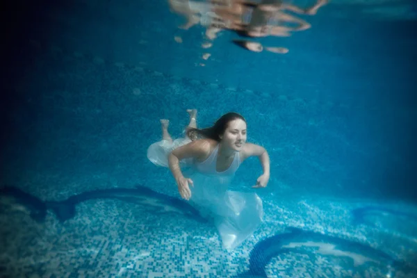 Mujer en vestido blanco subiendo a la superficie del agua en la piscina — Foto de Stock