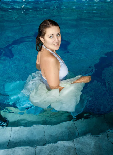 Mulher sorridente em vestido branco andando na piscina — Fotografia de Stock