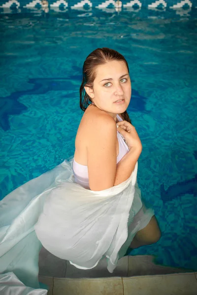 Morena mujer de pie en la piscina y cubierta con tela blanca — Foto de Stock