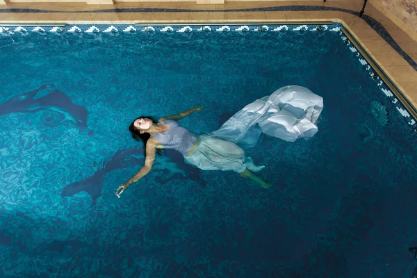 Женщина в длинном белом платье плавает на поверхности воды при плавании — стоковое фото