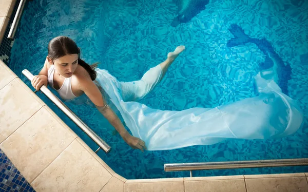 Mulher de vestido branco nadando ao lado da borda na piscina — Fotografia de Stock