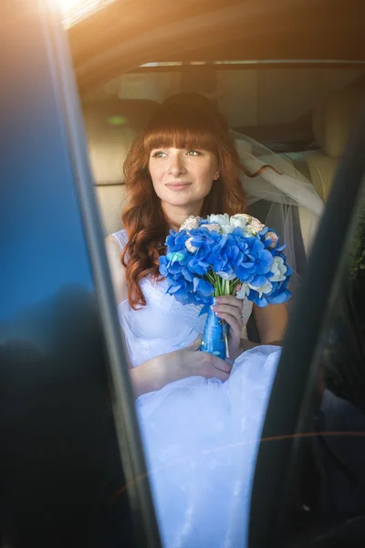 Schöne rothaarige Braut sitzt am sonnigen Tag am Auto — Stockfoto