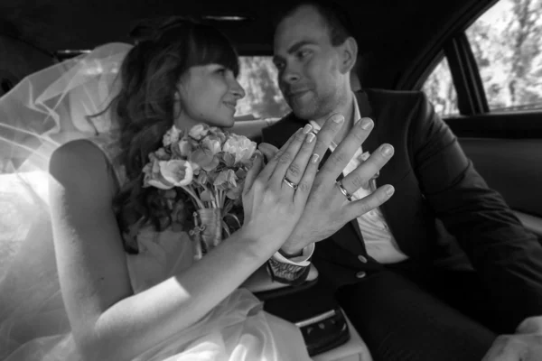 Bruid en bruidegom zitten in auto en tonen verlovingsringen — Stockfoto