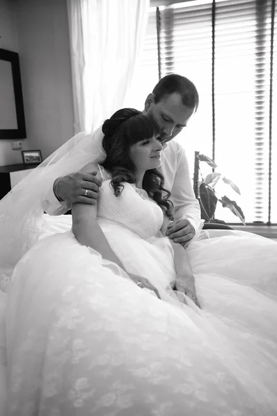 Monochrome portrait of bride and groom hugging on bed against wi — Stock Photo, Image