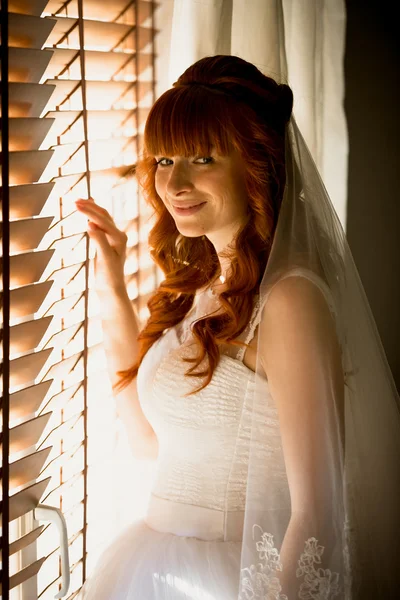 Young bride opening jalousie at sunny day — Stock Photo, Image