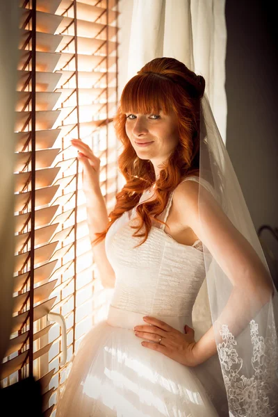 Portrait of beautiful redhead bride posing at window with jalous — Stock Photo, Image