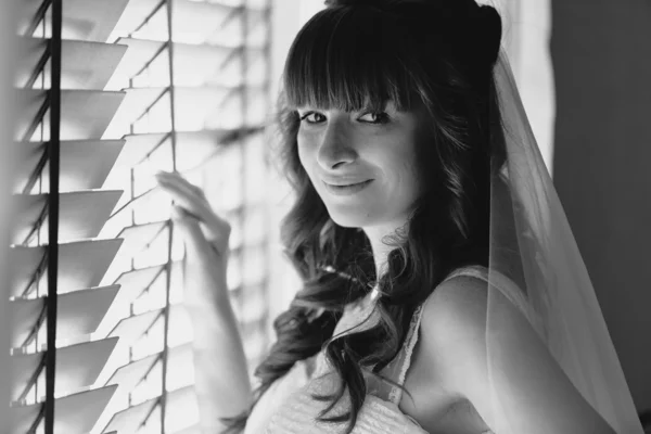 Monochrome portrait of cute smiling bride standing at window — Stock Photo, Image