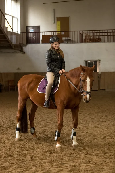 Jonge vrouw rijden bruin paard in overdekte manege — Stockfoto