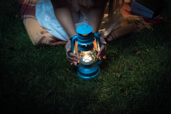 Женщина, сидящая на траве ночью и держащая за руки фонарь
