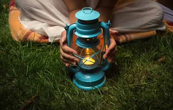 Woman sitting at garden at night and warming hands on lantern — Stock Photo, Image