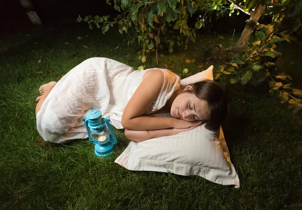 Mujer joven en camisón durmiendo en la hierba en el jardín por la noche — Foto de Stock