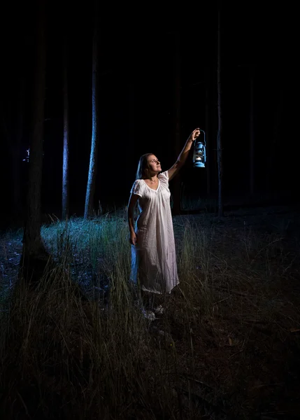 Женщина с газовым фонарем освещает лес ночью — стоковое фото
