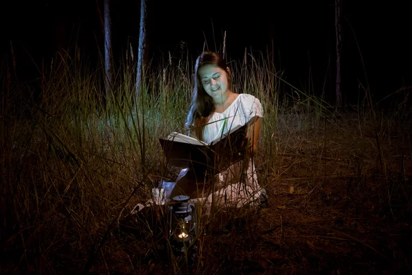 Mujer joven leyendo libro de magia en el bosque nocturno oscuro —  Fotos de Stock