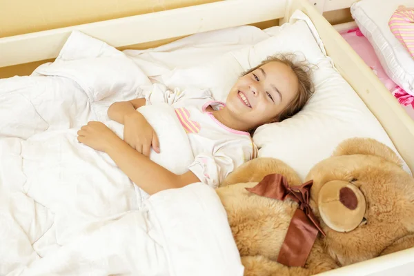 Улыбающаяся девушка лежит на кровати с большим плюшевым мишкой — стоковое фото