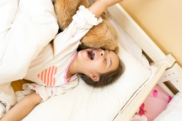 Jong meisje geeuwen in bed en stretching handen — Stockfoto