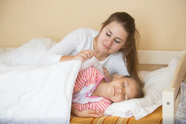 Matka, leżąc w łóżku z córką i obejmujący jej koc — Zdjęcie stockowe