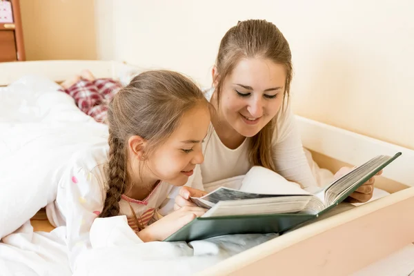 Mãe lendo grande livro velho para filha na cama — Fotografia de Stock