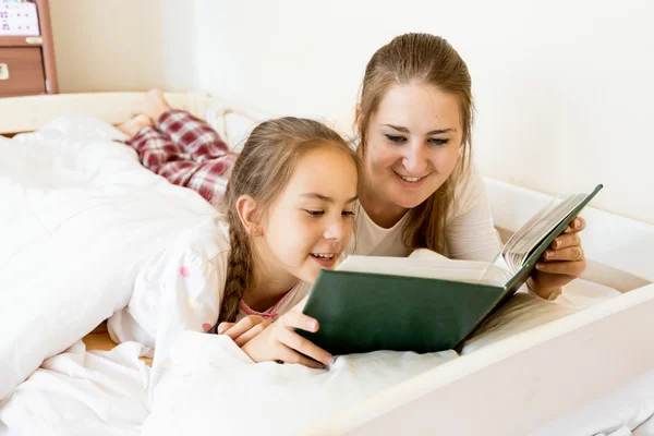 Portrét matky s dcerou na posteli ležel a čtení knihy — Stock fotografie