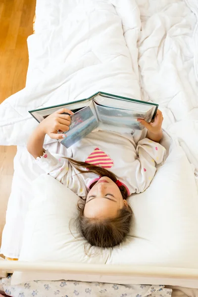 Little girl lying at bed in morning and reading big book — Stock Photo, Image