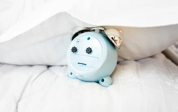 conceptual photo of alarm clock under pillow on bed