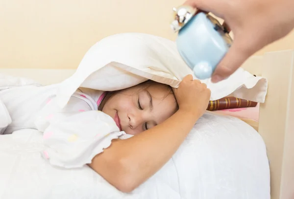 Foto de la madre sosteniendo el despertador en el oído de las hijas dormidas —  Fotos de Stock