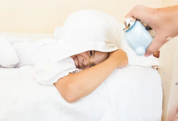 Chica cubriendo la cabeza con almohada y siendo despertado por el despertador — Foto de Stock