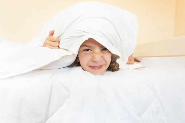 Portrait of little angry girl lying in bed with pillow on head — Stock Photo, Image