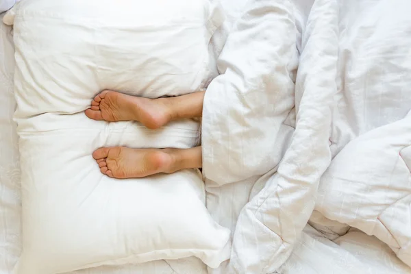 Feet lying on soft white pillow at bed — Stock Photo, Image
