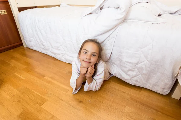 Petite fille couchée sous le lit à la maison et regardant la caméra — Photo