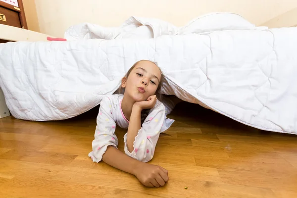 Young little girl lying on floor at bedroom under bed — Stock Photo, Image