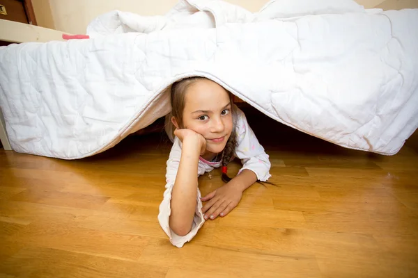 Kleines Mädchen liegt auf dem Boden unter dem Bett — Stockfoto