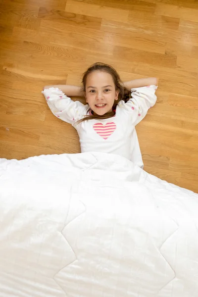 Smilende jente dekket med teppe liggende på tregulv – stockfoto