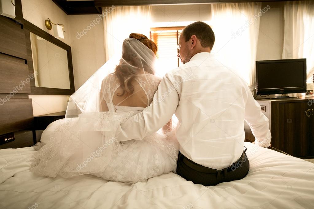 bride and groom sitting on bed and hugging