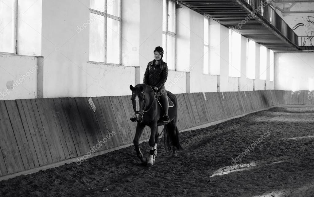 Black and white photo of woman riding horse at indoor manege