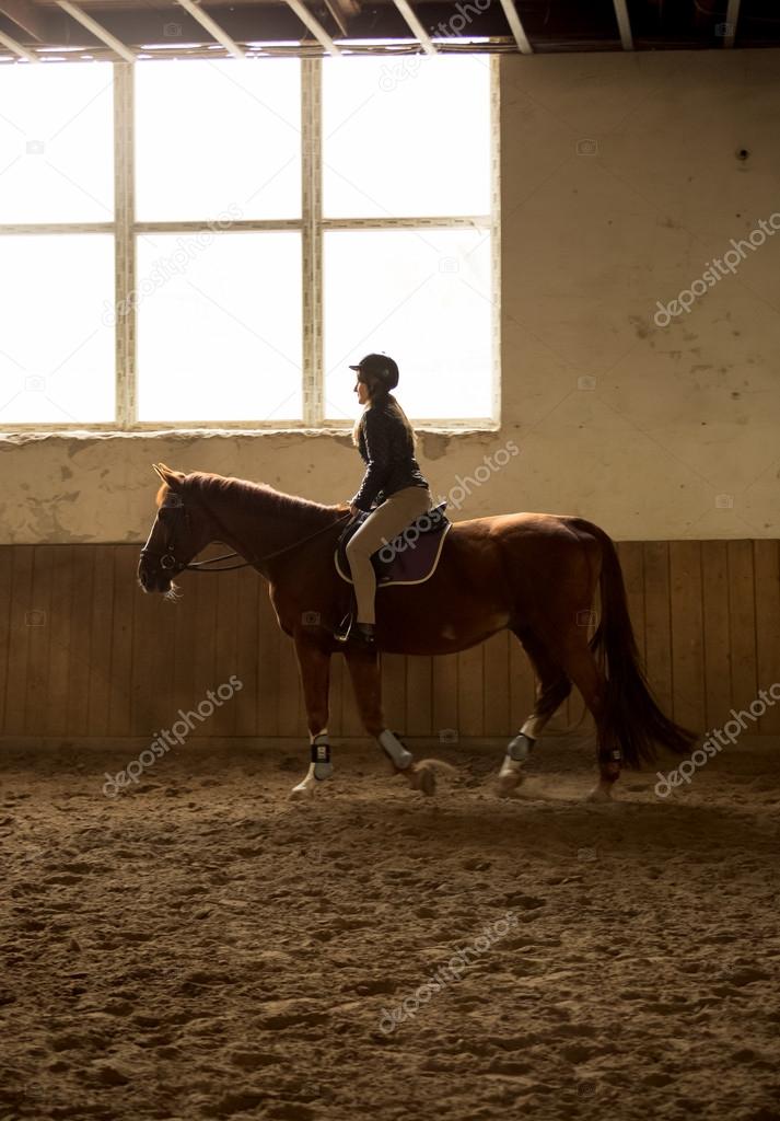woman riding horse at indoor manege with big window
